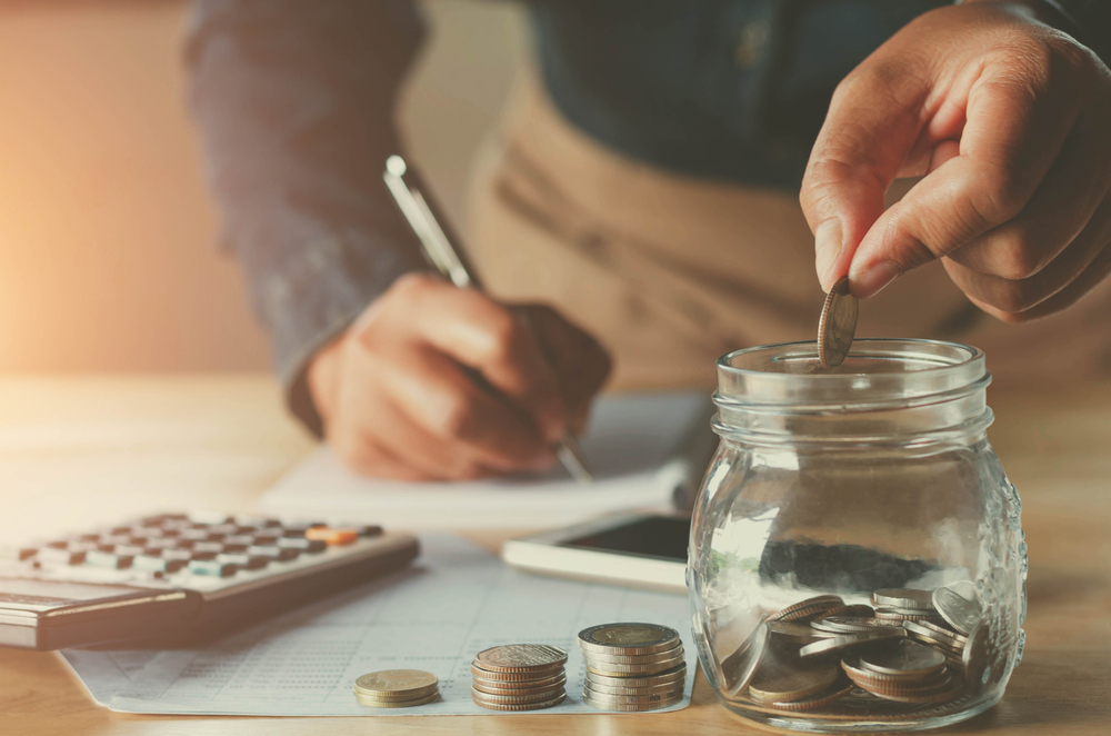 saving money with hand putting coins in jug glass concept